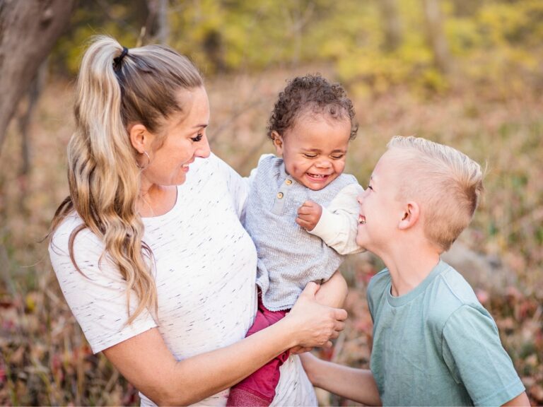 Adoption is a great alternative if you're not ready to become a full-time mother. An adoptive mother holds her adoptive son while her other son looks up laughing.