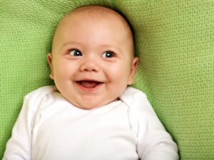 Understanding infant adoption brings joy all parts of the process. A smiling baby on a green blanket.