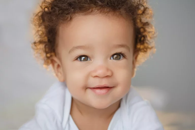 A baby with medium skin tone is smiling at the camera.