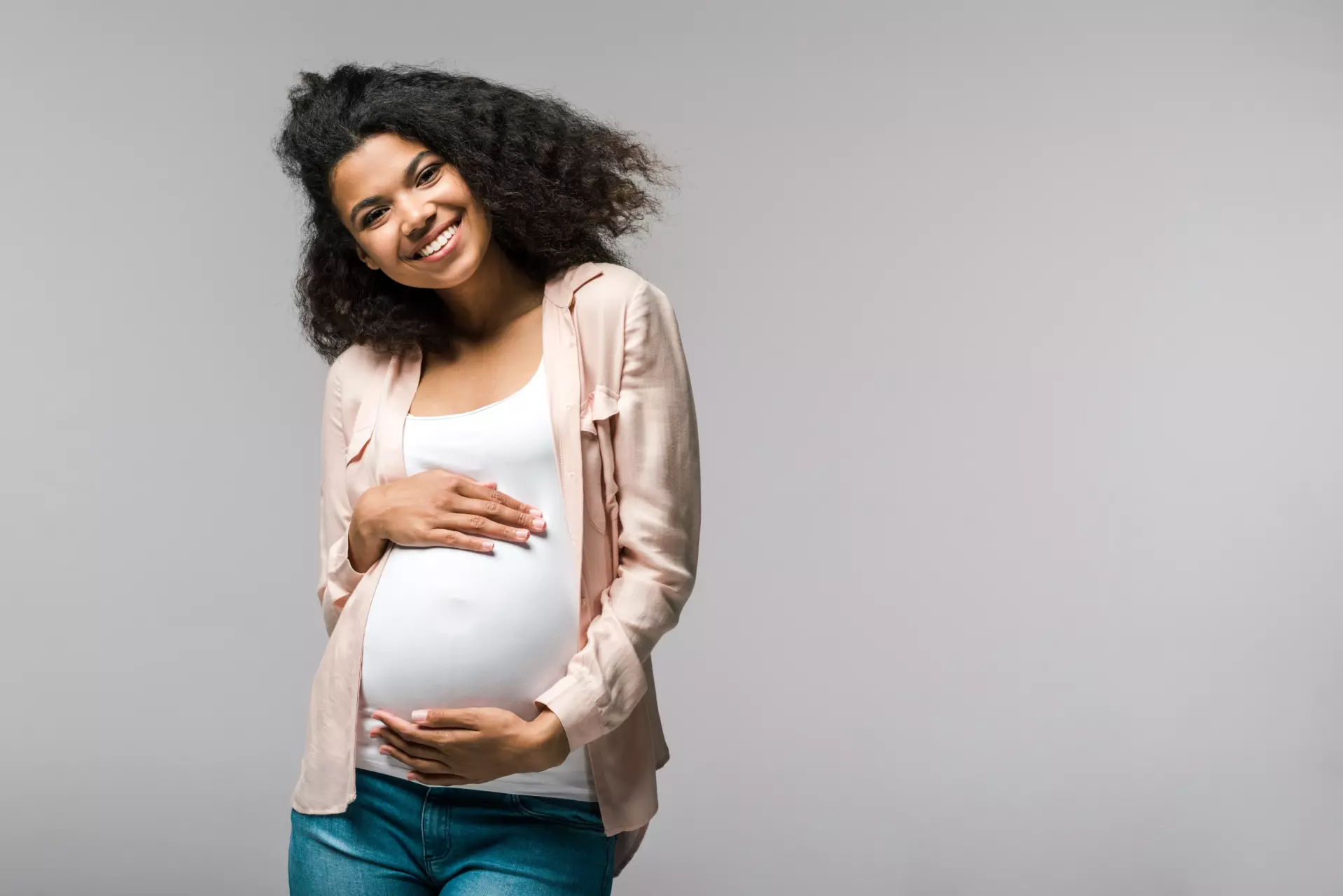 A pregnant woman holding her stomach and smiling into the camera.