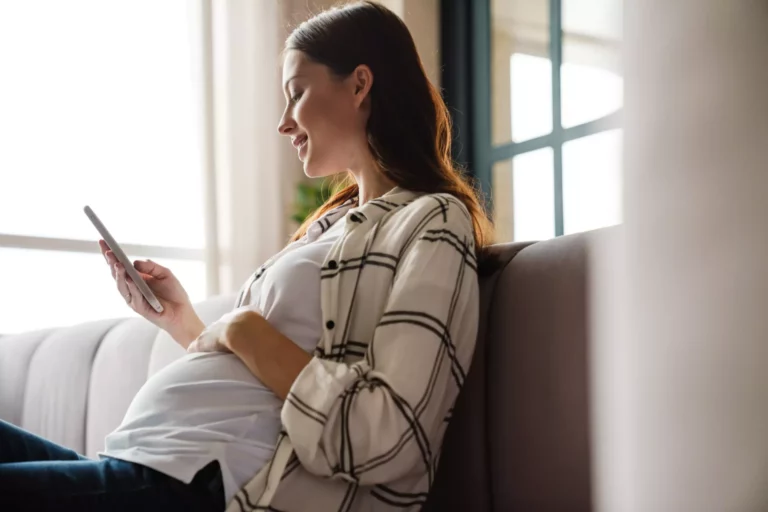 A pregnant woman sitting on a couch looking at her phone.