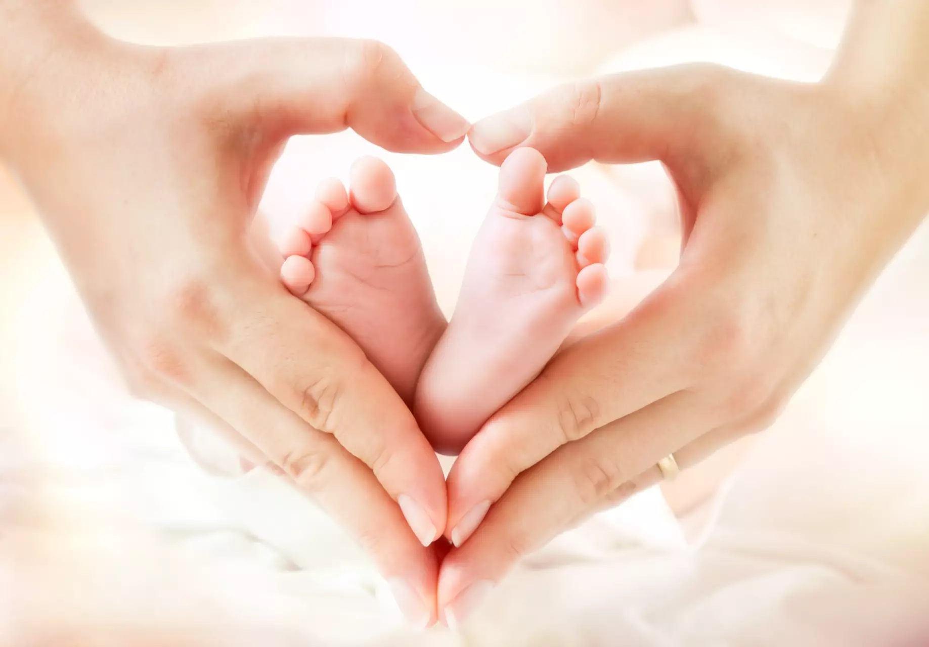 Two hands pressed together to make the shape of a heart. Inside the heart are a baby's two feet.