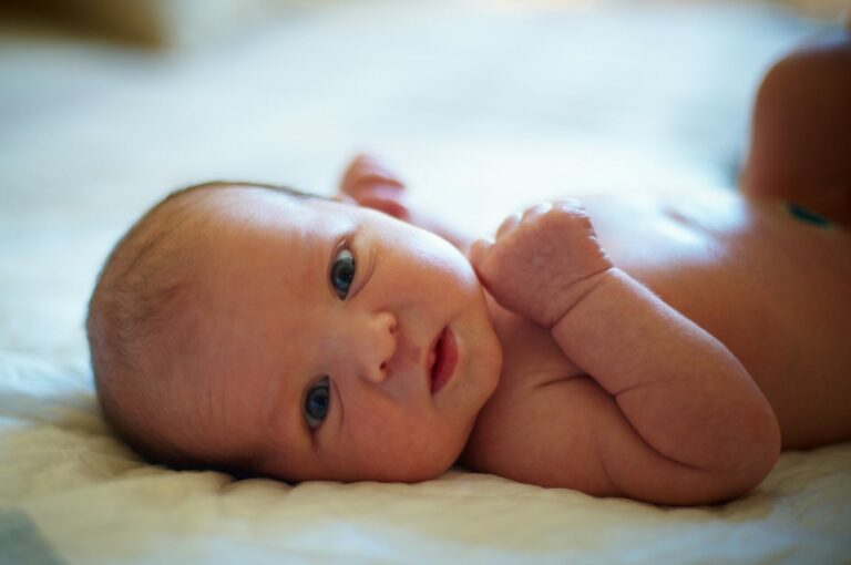 A newborn baby laying on its back and looking at the camera