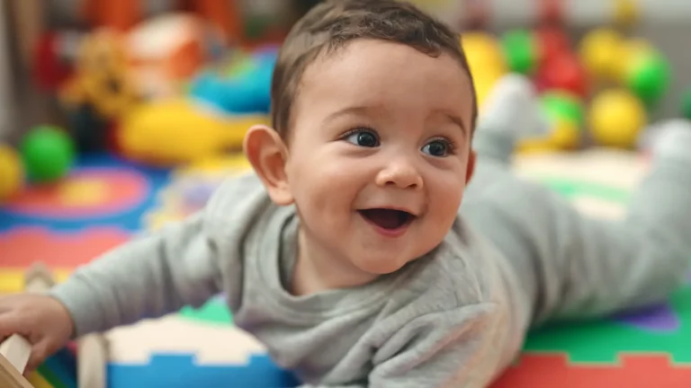 A smiling baby laying on their stomach on a colorful play mat.